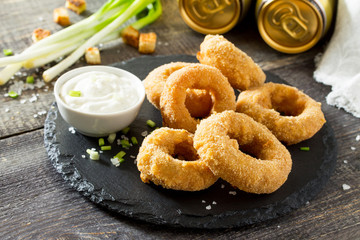 Onion rings fried with cheese on slate board. Snack food to beer on a wooden table.