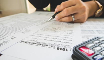 Business woman hand hold pen fill in the details on the tax forms paper in business concept