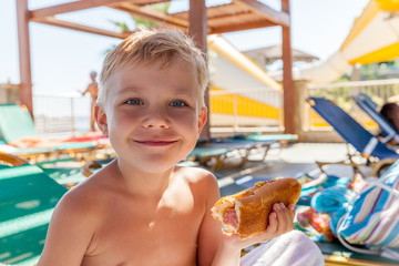 Adorable boy eating hot dog at the beach aquapark