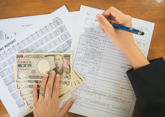 Woman hand hold pen fill in the details on the tax forms paper with yen moneyin business concept.