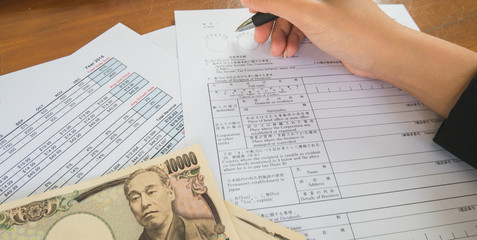 Fototapeta premium Woman hand hold pen fill in the details on the tax forms paper with yen moneyin business concept.