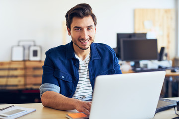 Creative young men working on laptop in office, typing on his computer and smiling