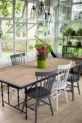 Dining room interior with table, chairs and plants against big windows
