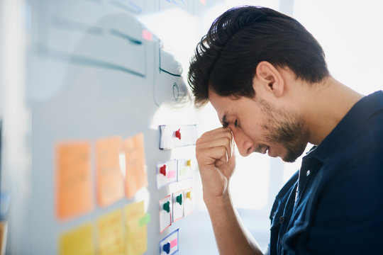 Frustrated, stressed designer struggle for new project ideas banging his head against whiteboard at office
