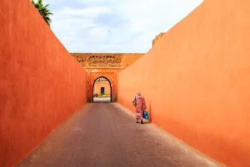 Tuinposter Muslim woman walking through a narrow street with gate in Marrakech © pwollinga
