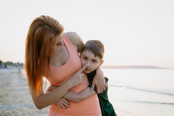 Fototapeta na wymiar Mother and son staying and hugging at the sea coast during sunrise or sunset
