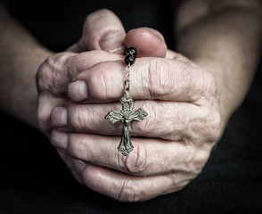 Hands clasped in prayer holding a rosary with a metal cross symbolizing faith, spirituality, hope and religious devotion