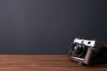 Old retro camera in leather case on vintage wooden boards black background
