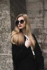 Fashionable blonde model in glasses near a brick wall