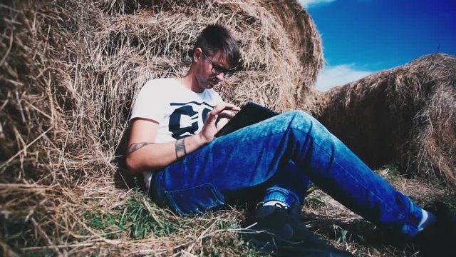 Man in jeans working on a laptop in a haystack