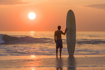 surfer silhouette at sunset with longboard