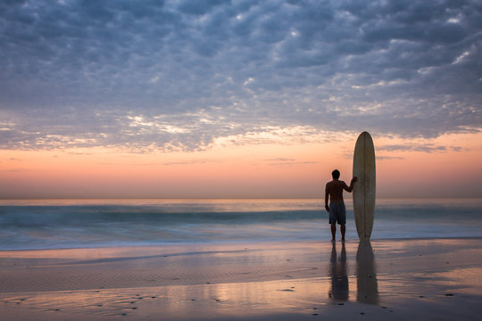 surfer silhouette at sunset with longboard
