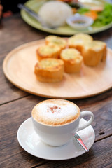 Coffee late with garlic bread on wood plate.