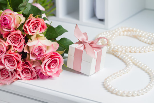 Gift box with pink ribbon with pearl jewellery necklace and roses on white table