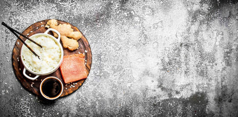 Asian food. Boiled rice with a piece of salmon and soy sauce. On rustic background .