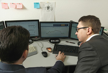 Two men working together for the computers in the office engaged in trading