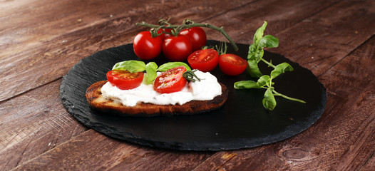 Bread with cream cheese and tomato for lunch table. Sharing antipasti on party or summer picnic time over wooden rustic background.