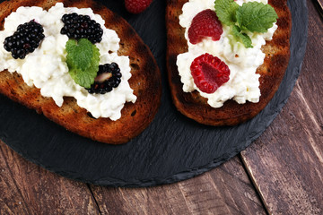 Bread with cheese cream and blackberries and raspberries for lunch table. Sharing antipasti on party or summer picnic time over wooden rustic background.