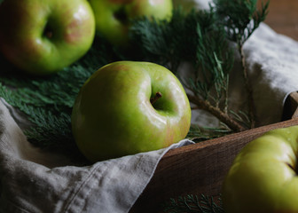 Close-up of a large harvest ripe green apples on the background of fir branches and flax napkin in a wooden box