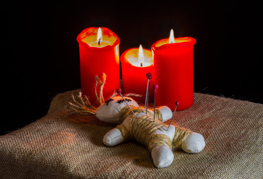 eine Voodoopuppe liegt neben brennenden Kerzen auf einem Tisch