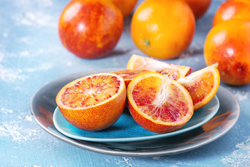 Sliced and whole ripe juicy Sicilian Blood oranges fruits on ceramic plate over blue concrete...
