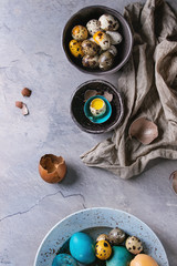 Colored Easter blue brown chicken and quail eggs, whole and broken with yolk in shell in spotted plate and black bowls with textile over gray textured background. Top view with space