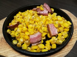 Stylist food, fried sweet corn bacon and chop parsley with butter and seasonings serve on the hot pan plate focus-on-foreground with blur background
