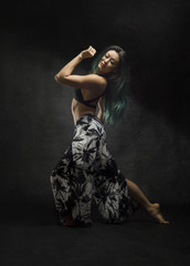 beautiful strong asian with long green hair dances with sensual dramatic graceful poses on dark textured background  
