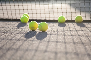 Six tennis balls are near net on tennis court during sport playing at sunset.