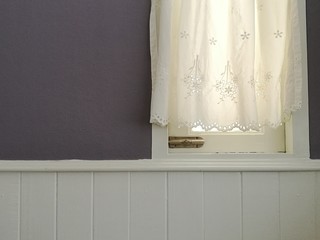 White Lace satin curtain hanging on window with sunlight semitransparent, vintage light purple wall and white siding decoration interior room