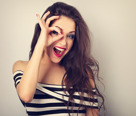 Beautiful emotional laughing woman showing glasses gesture by the fingers with open mouth and...