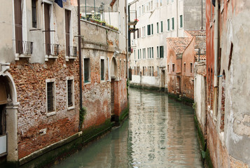The river flows through the narrow streets of Venice between old houses in Italy
