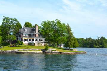 Island with house, cottage or villa in Thousand Islands Region in sunny summer day in Kingston, Ontario, Canada. 1000 Islands near Gananoque, ON. Famous Canadian tourist vacation routs. - obrazy, fototapety, plakaty