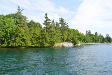 Fototapeta na wymiar 1000 Islands Region. Sunny summer day. Rocky Island on the St. Lawrence River crowned with pine trees. Kingston, Ontario, Canada. Unfiltered, natural lighting. Tourist routs.