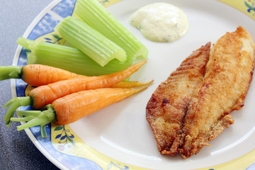 decorated plate with fried fish: river trout filet with carrots, celery and sauce, served
