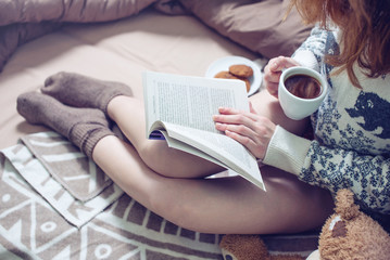 girl reading book in bed with warm socks drinking coffee