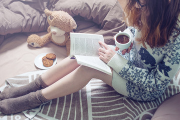 girl reading book in bed with warm socks drinking coffee