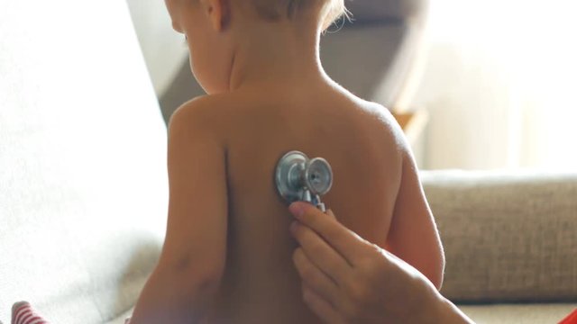 Kid doctor examing little baby boy with stethoscope in a sunny room