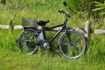 Fototapeta na wymiar Electric bicycle on the wood fence in the park on sunny summer day. Shot from the side. Unfiltered, with natural lighting. The view of the e motor, power battery and gear.