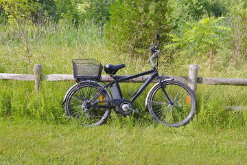 Fototapeta premium Electric bicycle on the wood fence in the park on sunny summer day. Shot from the side. Unfiltered, with natural lighting. The view of the e motor, power battery and gear.