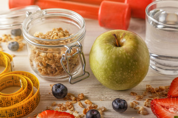 Healthy breakfast, dumbbells and measuring tape on wooden backgr