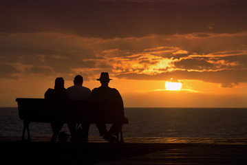 Fototapeta na wymiar Silhouette of a group of seniors who sits on the bench, looking at the sunset