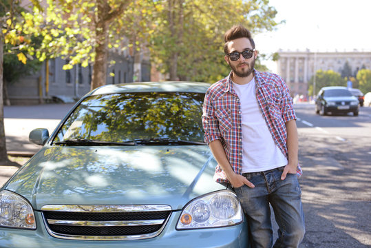 Successful young man standing near car