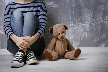 Little girl sitting with toy bear on color wall background