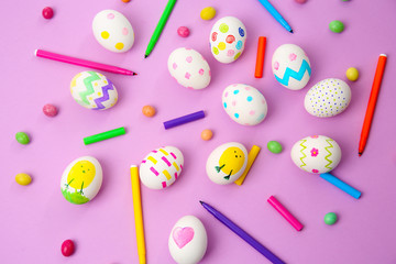 Composition with painted Easter eggs, candies and felt pens on color background