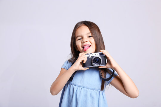 Little girl with vintage camera on light background