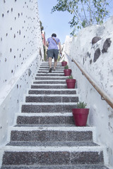 Mężczyzna chodzi w górę białkujących kamiennych schodków w Santorini, Grecja - 138608860