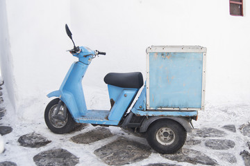 jasnoniebieski skuter motorowerowy zaparkowany przed bieloną ścianą na ulicach Mykonos w Grecji - 138609415