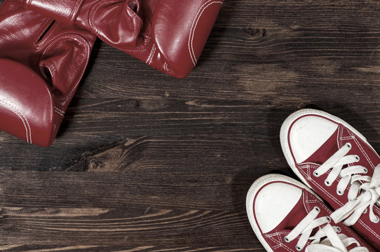 Red boxing gloves and red sneakers on a wooden surface