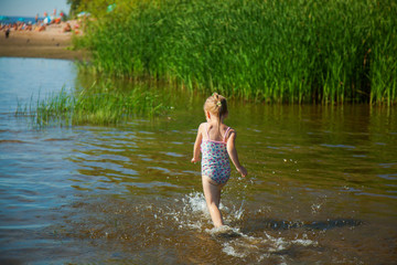 Cute little girl runs in warm water in river on a hot sunny day